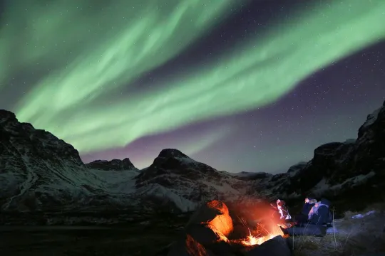 Guests sitting by a bonfire under the northern lights